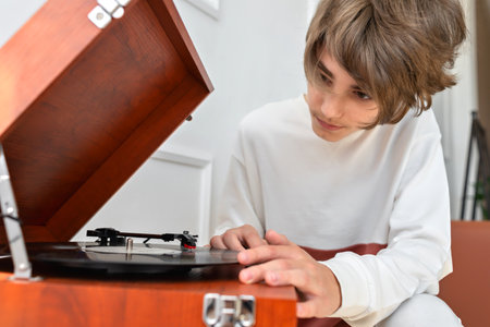 Handsome teenager boy in white shirt turning on retro vinyl player, brown wooden turntable, listening music, lifestyleの写真素材