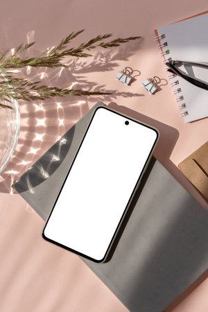 Minimalist aesthetic stationery flatlay, business brand template, copy space. Blank smartphone screen mock up, notebook, paper cards, glasses on pastel pink background with sun light shadow.の写真素材