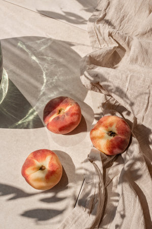 Ripe peach fruits on neutral beige tabletop, linen tablecloth, aesthetic floral sunlight shadow. Elegant sustainable lifestyle background, healthy vitamin food conceptの写真素材