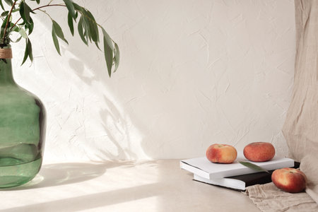 Aesthetic home interior design template, vase with tree branches, peaches, book, glasses on table, empty beige wall background with sunlight shadowの写真素材