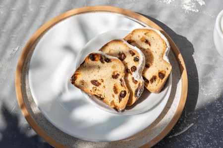 Christstollen, Christmas stollen sliced on pieces on a plate with aesthetic floral sunlight shadows, sweet fruit cake with raisins, bakery for winter morning breakfast, lifestyle flatlayの写真素材
