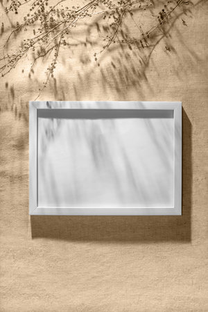 White frame mockup on a warm beige wall with aesthetic floral sunlight shadows and dried grass, elegant business, branding template with copy spaceの写真素材