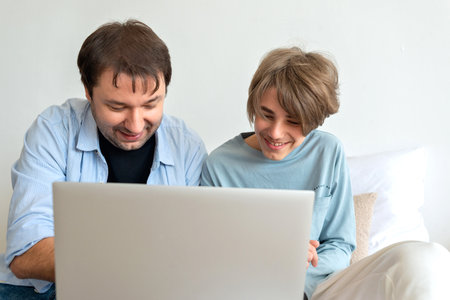 Single father and teenager son communicate online, in a social media, making video call or watching video, playing game together. Happy family relations, fatherhood, parent support and care of childの写真素材
