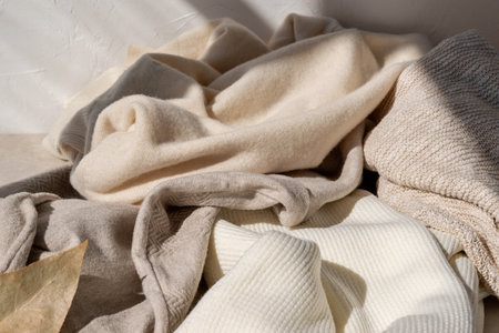 Messy crumpled warm wool and cotton neutral beige pastel knitted clothes, knitwear in sunlight with shadow. Fall season woman fashion wardrobe conceptの写真素材