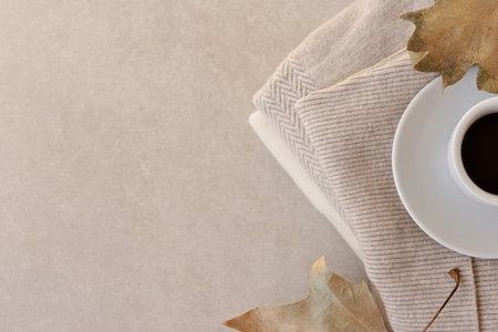 Aesthetic minimalist autumn background, hot coffe cup, cozy ktitted sweaters, dried leaves on neutral beige pastel backdrop, flat lay, copy spaceの写真素材