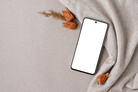 Blank mobile phone screen mockup on neutral beide, nude color knitted textile background, fall ginger red, terracotta dried flowers. Aesthetic autumn business brand template, , flat layの写真素材