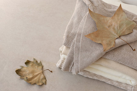 Wool knitted sweaters stack in neutral nude colors, light brown fall leaves on beige table. Minimalist fashion clothes wardrobe, stylish jersey knitwearの写真素材