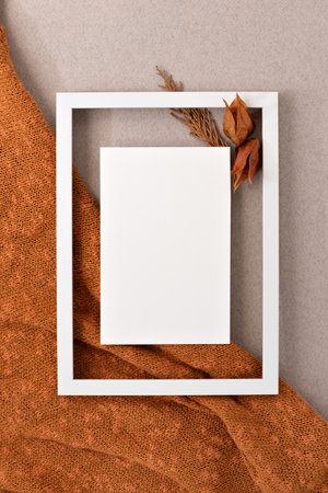 Blank paper card mock up in empty picture frame, dried orange flowers on ginger knitted textile and neutral beige background. Aesthetic autumn business brand template, wedding invitation designの写真素材