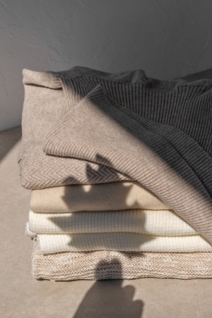 Autumn aesthetic woman fashion wardrobe concept. Neutral beige knitted clothes stack with a fall leaf sunlight shadow silhouette. fashion blog design templateの写真素材