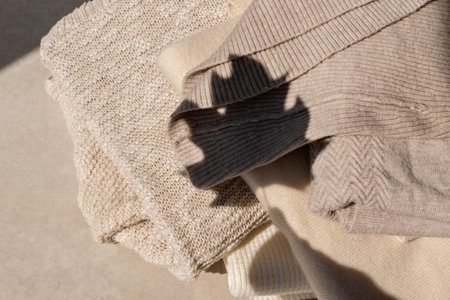 Neutral beige knitted sweaters on a beige background with aesthetic fall leaf sunlight shadow silhouette. Autumn woman clothes wardrobe concept, lifestyleの写真素材