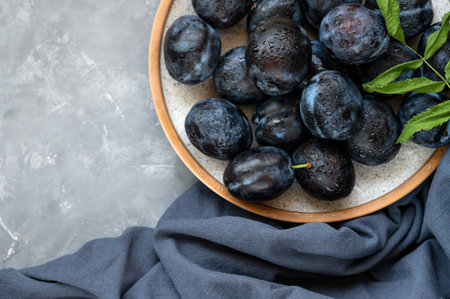 Ripe plum fruits on plate with water drops, on dark blue tablecloth and gray background. Aesthetic flat layの写真素材