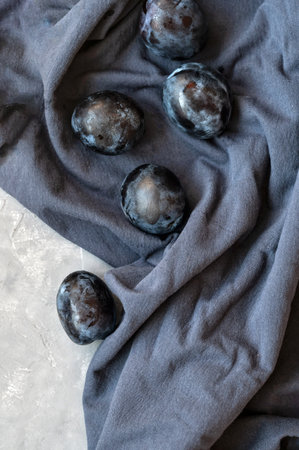Some ripe plum fruits on dark blue crumpled tablecloth background. Aesthetic still life, flat lay.の写真素材