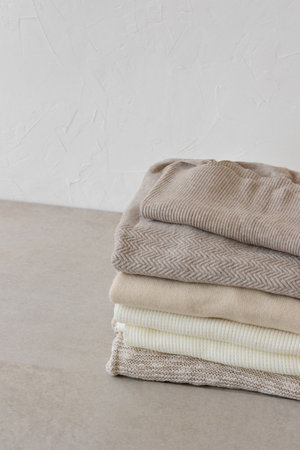 Aesthetic fashion minimalist wardrobe concept, warm autumn knitwear jersey. Wool knitted clothes stack closeup in neutral beige colors on table on white empty wall backgroundの写真素材