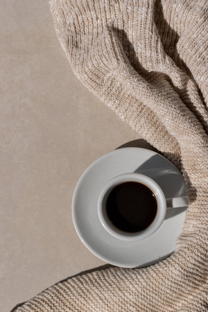 Hot coffee drink cup on neutral beige table background with light brown knitted cloth in sun light. Minimalist aesthetic morning coffee, cozy autumn concept. Flat lay, copy space.の写真素材