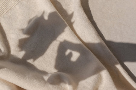 Fall leaf in woman hand, sunlight shadow silhouette on crumpled knitted beige, milky color cloth background. Aesthetic autumn concept.の写真素材