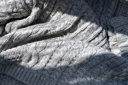 Natural lifestyle sunlight shadow on crumpled knitted neutral gray cloth with cable stitch pattern, cozy minimalist winter or fall background.の写真素材