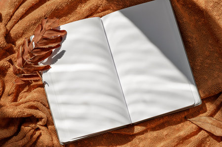 Open notebook blank with empty sheet mock up, dried fall leaf on knitted rust color cloth background...