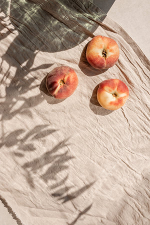 Peaches on beutral beige linen tablecloth background with floral sunlight shadows.