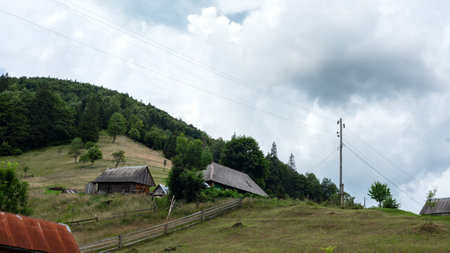 Authentic Ukrainian small mountain village with wooden houses and outbuildings in a hill near forest. Countryside in Carpathian mountains, Ukraine.の写真素材
