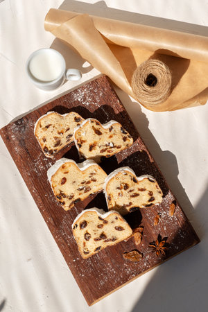 Christstollen, stollen sliced on pieces on a wooden board, cup with milk on beige table background...