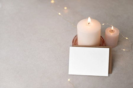 Plank paper card mockup, defocused candles and garland lights on neutral beige table background. Aesthetic Scandinavian winter Christmas postcard or invitation design template.の写真素材