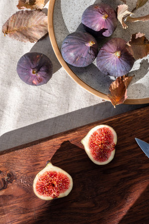 Whole and cut fig fruits on plate and wooden cut board, on linen tablecloth with natural sunlight shadows. Healthy sweet autumn food, vitamin dessert for fall diet.の写真素材