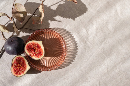 Aesthetic fig fruit autumn composition, cut fig on plate with dried leaves and natural sunlight shadows on neutral beige linen tablecloth. Lifestyle, fall healthy vitamin food, diet concept.の写真素材