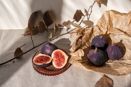 While and cut fig fruits on neutral kitchen table with dried fall leaves and natural sunlight shadows, lifestyle.の写真素材
