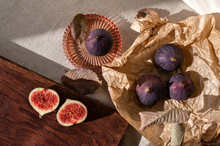 Cut fig on wooden board, whole fig fruits on crafted paper. Kitchen table with linen tablecloth and autumn fruits, lifestyle food flat lay with natural sunlight shadows.の写真素材