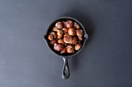 Roasted chestnuts in pan on dark gray, black background. Minimal stylish flat lay, traditional Christmas authentic food.の写真素材