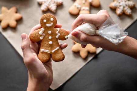 Christmas gingerbread man cookie decoration with sugar icing. Person's hands holding gingerbread man cookie and piping bag with sugar icing, making ornament. Holiday homemade family bakery.の写真素材