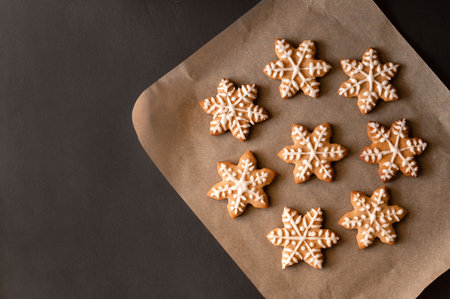 Christmas snowflake or star shape gingerbread cookie decorated with sugar icing on parchment on dark...