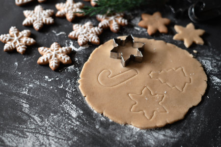Rolled dough on table with snowflake, Christmas tree and cane ornaments of cookie cutters, baked snowflake cookie on black table background with flour. Soft selective focus, lifestyle.の写真素材