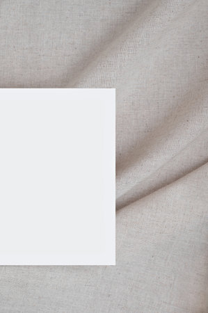 Blank paper card mockup on soft blurry crumpled linen neutral beige fabric background with folds and natural shadows, elegant wedding invitation or business card branding template.の写真素材