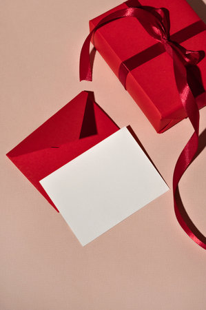 Blank paper card, red envelope and gift box on pastel peach background with harsh light shadows. Luxury holiday celebration backdrop, business branding template, invitation or greeting postcardの写真素材