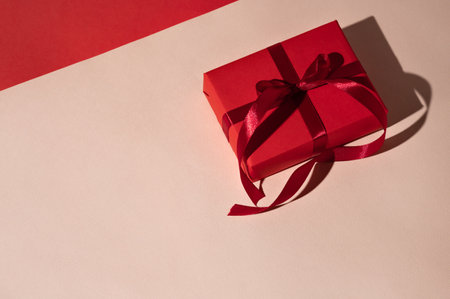 Festive holiday business branding template with red gift box on light peach and red background with harsh shadows, copy spaceの写真素材