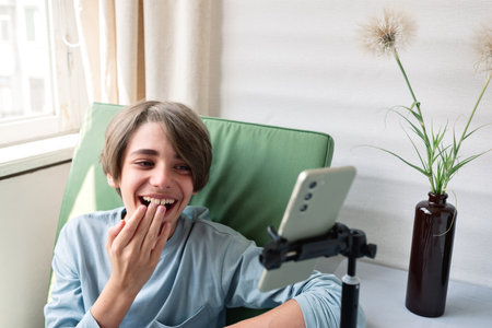 Teenager boy watching video or webinar online on his smartphone and laughing, youth in cyberspace,...