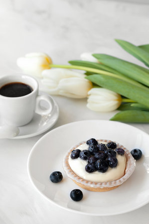 Panna cotta with blueberries on plate, cup of coffee and flowers on white table, traditional Italian sweet milky dessert.の写真素材