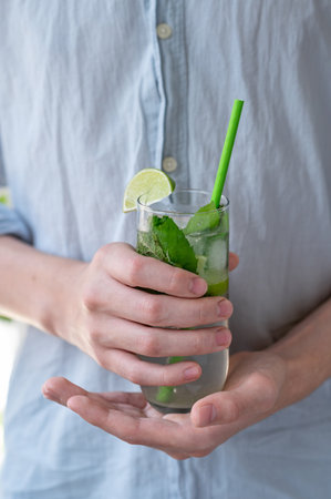Person wearing blue shirt holding glass with mojito cocktail drink.の写真素材