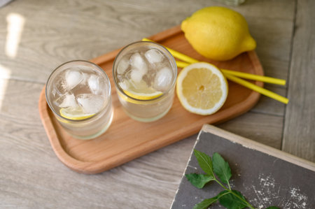 Two glasses with iced lemonade drink on wooden tray with yellow lemons and drinking straws, neutral beige table background, top view, soft selective focus, lifestyle.の写真素材