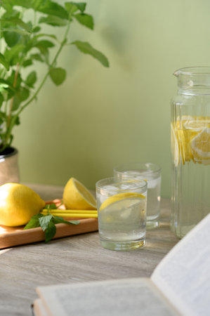 Aesthetic summer food and drink background, lemons, mint, open book, glasses and jug with lemonade iced beverage on brown wooden table, soft green backdrop.の写真素材