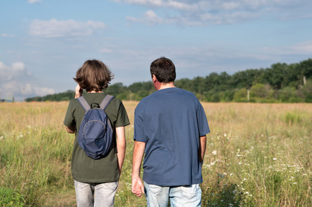 Teenager boy and his father hiking outdoors in countryside on sunny summer day, back view.の写真素材