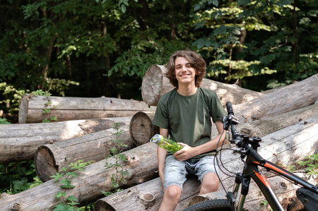 Teenager boy sitting on logs in forest near bicycle, happy smiling young man have a break during bike ride outdoor.の写真素材
