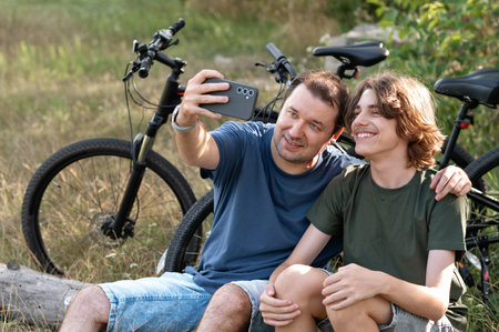 Father and his teenager son taking selfie on mobile phone while walking and cycling in nature.の写真素材