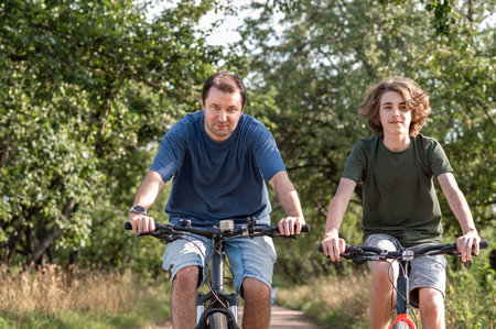 People riding on bicycles outdoor in nature, father and son cycling together in park.の写真素材