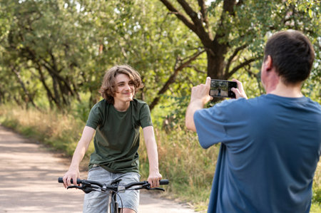 Father taking photo of his teenager son on smartphone during bike ride in nature.の写真素材