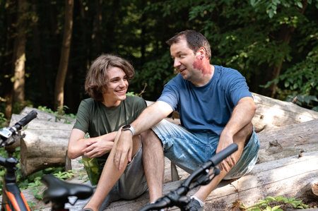 Father and teenager son sitting in forest, talking and smiling during walk in nature outdoor.の写真素材