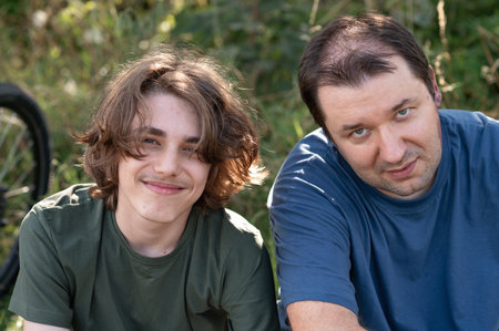 Father and his teenager son sitting in nature and looking at camera.の写真素材