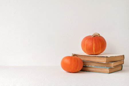Old books and orange pumpkins on neutral beige table and white wall background with empty copy space, fall aesthetic backdrop, Halloween, Thanksgiving, knowledge day concept design.の写真素材