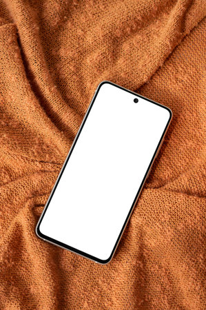 Mobile phone with blank screen mockup on ginger orange color knitted fabric background, lifestyle autumn design template for business branding or social media.の写真素材